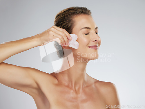 Image of Beauty, face and massage with a woman using a gua sha or scraping tool in studio on a gray background for skincare. Wellness, skin and body with a mature female taking care in her antiaging routine