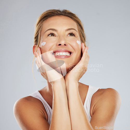 Image of Face, beauty and skincare with a beautiful woman in studio on a gray background for antiaging or healthcare. Health, body and care with a mature female applying lotion or cream to her skin