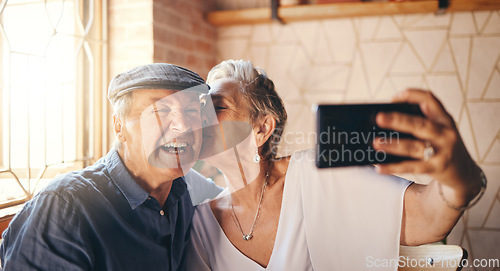 Image of Love, phone and selfie with elderly couple kiss and relax in their home together, laughing and bonding. Photography, retirement and seniors enjoying retired lifestyle and romance in their living room