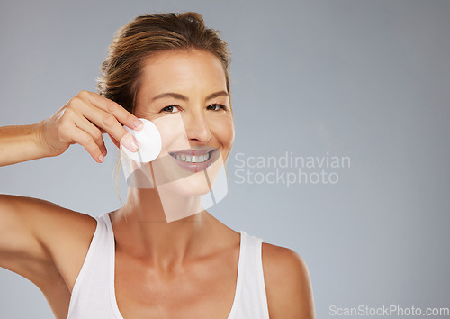 Image of Skincare, mature woman and facial cotton cleaning face, makeup or cosmetics removal on a gray studio background. Wellness, health and female model with skin cleanser, beauty treatment or exfoliation
