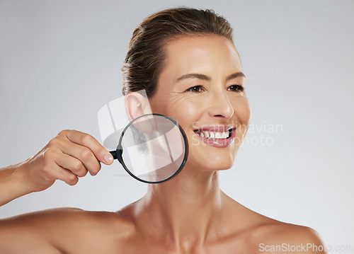 Image of Mature woman, skincare and smile magnifying glass to zoom on face for health, wellness and facial beauty. Model, happy and skin show happiness with natural glow against cosmetics studio background