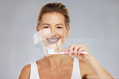 Image of Teeth, dental and oral hygiene with a woman brushing using a toothbrush and toothpaste in a studio on a gray background. Health, healthcare and face with a female taking care of her mouth and gums