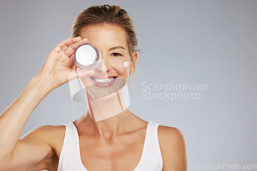 Image of Beauty, skincare and product with a woman advertising or marketing antiaging skin treatment in studio on a gray background. Cosmetics, body and care with a beautiful mature female holding a container