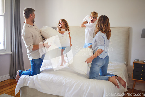 Image of Family pillow fight, in parents bedroom and kids smile with happiness. Children jump on a bed, playing with mom and dad at home. Happy bonding time, having crazy fun and laughing together with energy