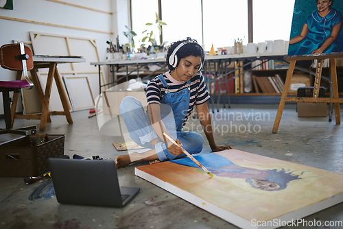 Image of Laptop, woman artist and painting on floor in studio, gallery or workshop with headphones and streaming music for inspiration. Creative, girl or lady in workspace listen to podcast or focus on canvas