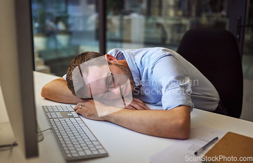 Image of Burnout, tired and sleep with a business man sleeping on his desk while working on a computer at a desk in his office. Mental health, problem and exhausted with a young male employee at work at night