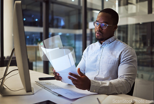 Image of Night worker, black businessman and paperwork planning, reading documents and financial reports at desktop computer in Jamaica. Young focus entrepreneur working expert strategy in dark modern office