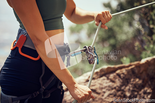 Image of Fitness, safety and hands of rock climbing woman with security, harness cable or sport equipment on mountain cliff. Travel, hiking or adventure girl exercise with mountaineering rope workout training