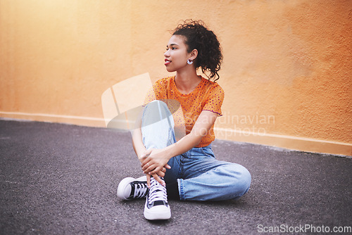 Image of Fashion, sneakers and young woman on street in the city. Portrait of urban, trendy and black female model against an orange wall background sitting on the road. Style, clothes and girl posing