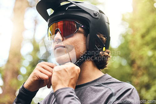 Image of Fitness, helmet and man cycling in nature on his bicycle outdoors for exercise, training and workout in spring. Sports person riding a bike and fixing headgear on an adventure in the forest or woods
