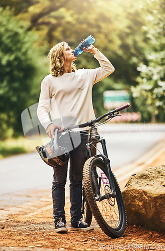 Image of Health, cycling and woman drinking water on a break in nature to hydrate, wellness and resting outdoors. Sports, exercise and thirsty biker riding bicycle by the road refreshing with liquid