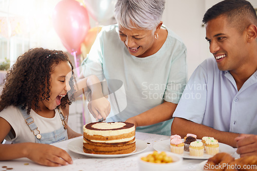 Image of Birthday, cake and girl at party with grandmother cutting dessert with father in celebration at living room table in house. Wow face on child with sweet food, tart and candy to celebrate with family