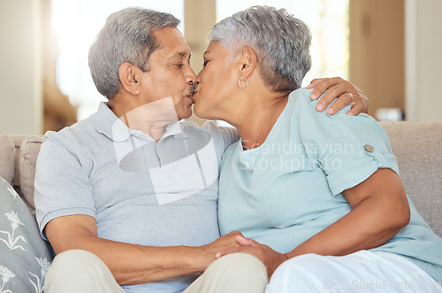 Image of Senior couple, kiss and love at home while sitting on sofa in lounge to bond, relax and enjoy free time during retirement. Old man and woman sharing romantic and sweet moment in their Mexico house