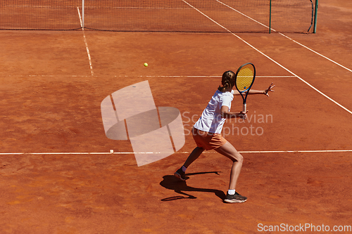 Image of A young girl showing professional tennis skills in a competitive match on a sunny day, surrounded by the modern aesthetics of a tennis court.