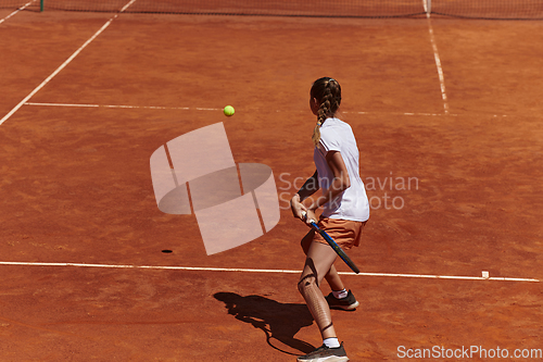 Image of A young girl showing professional tennis skills in a competitive match on a sunny day, surrounded by the modern aesthetics of a tennis court.