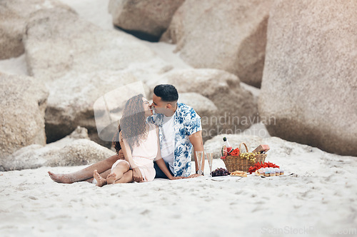 Image of Couple, beach and love on picnic, kiss and happy together on sand by rock. Man, woman and smile with happiness on face with lips, basket and flowers to relax, vacation and travel in summer in Sydney