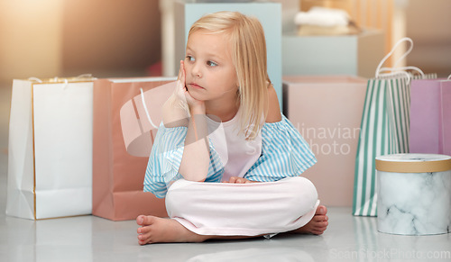 Image of Child, fashion and shopping bags while looking bored and waiting in a kids clothing shop, store or boutique with cute girl sitting on floor. Little kid shopper or customer with sale purchase packages