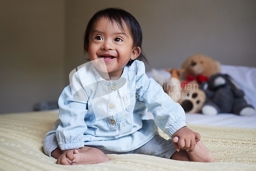 Image of Baby, down syndrome and special needs child happy with a smile sitting on a bed to relax, be curious and playful in bedroom at home. Cheerful girl with intellectual disability and developmental delay