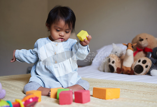 Image of Down syndrome, daycare and baby on the bed with toys, playing with color shapes and blocks. Child development, special needs and cute girl in bedroom learning, having fun and therapy games for kids