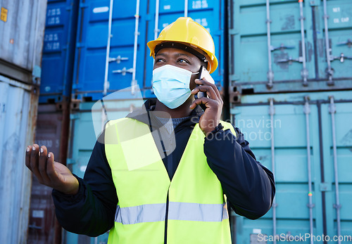 Image of Covid, logistics and black man on phone call while working at a container warehouse. African industrial manager talking about shipping, delivery and cargo on a mobile with a face mask at storage site