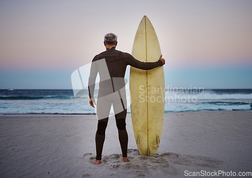 Image of Surf, sea and sport with a man on the beach with his surfboard looking at the ocean view or horizon at sunset. Health, fitness and sports with a male athlete standing in the sea by water in nature