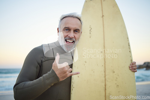 Image of Senior man, with surfboard and at beach smile, happy and at sunset with swimwear on a holiday and vacation. Portrait, shaka and older male surfer, hand sign and at seaside surfing while on a trip.