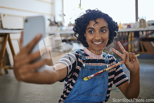 Image of Indian woman artist, selfie with paint brush and art on floor of studio workshop to share to social media. Portrait of happy, creative professional painter and smiling after oil or watercolor project