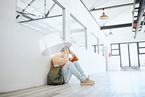 Image of Young man, mental health and stress student, depressed and on floor holding head in empty room. Burnout, male and frustrated with fear, social anxiety and anxious with tired, overworked and scared.