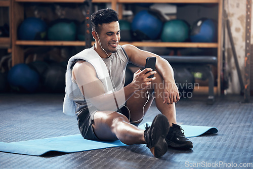 Image of Man, exercise and phone on social media with smile rest on floor in gym during training session. Guy, wellness and smartphone take break during workout for fitness, health and sport with happiness