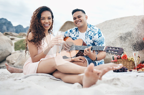 Image of Couple, beach and guitar for music and love on picnic together on sand by ocean. Man, woman and smile with happiness on face with food, champagne and flowers to relax, vacation and travel in summer