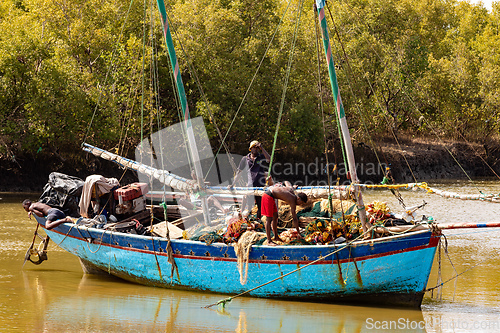 Image of Two men repair a fishing net on a blue boat moored to the riverbank in Morondava Madagascar