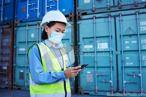 Image of Covid, social media and logistics worker reading chat on a phone working at a container factory. Asian industrial employee with face mask on web for shipping and delivery of cargo on mobile at a site