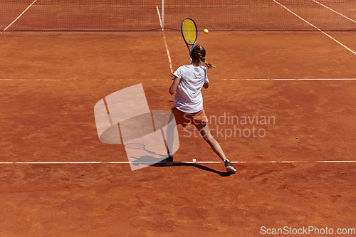 Image of A young girl showing professional tennis skills in a competitive match on a sunny day, surrounded by the modern aesthetics of a tennis court.