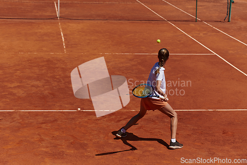 Image of A young girl showing professional tennis skills in a competitive match on a sunny day, surrounded by the modern aesthetics of a tennis court.