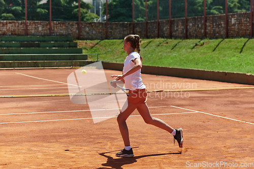 Image of A young girl showing professional tennis skills in a competitive match on a sunny day, surrounded by the modern aesthetics of a tennis court.