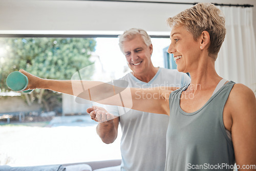 Image of Fitness, health and senior couple doing exercise in the living room of their comfortable home. Happy, smile and healthy elderly woman doing arm workout with motivation from her husband in retirement.