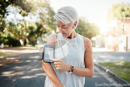 Image of Senior woman, fitness and phone armband listening to music for morning run in an urban street outdoors. Active elderly female runner checking smartphone to monitor training exercise or navigation