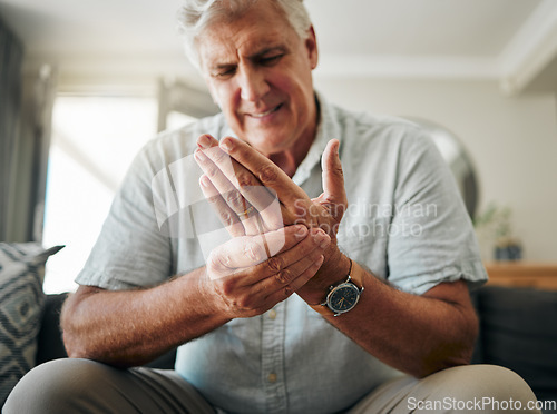 Image of Hands, pain and arthritis with a senior man holding his hand while suffering from osteoporosis, cramp or injury. Health, medical and joint with an elderly male pensioner in the living room at home