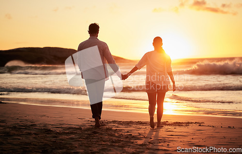 Image of Sunset, couple holding hands and walking by the beach with a beautiful twilight. Love, romance and happy man and woman spending time together with affection by ocean, sea and sandy shore on holiday.