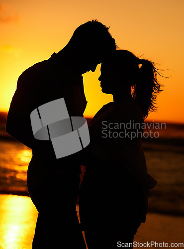 Image of Silhouette of young couple on the beach at sunset embracing each other in affection. People on holiday, vacation and honeymoon by the ocean. Intimate, love and romantic man and woman together by sea