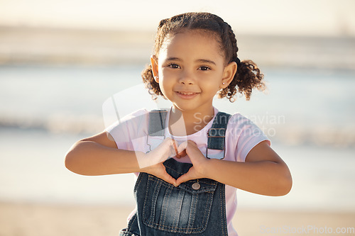 Image of Girl at beach make heart sign with hands, happy and smile against blurred nature background. Young female child with expression of happiness, makes love icon, gesture with fingers by the ocean or sea