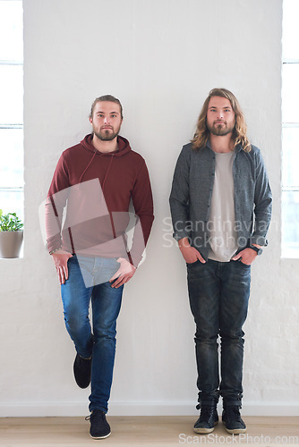 Image of Portrait of twin brothers standing by a wall together in studio. Young twins, siblings and family of young men side by side. Relationship with brother, brotherhood and two guys who look identical