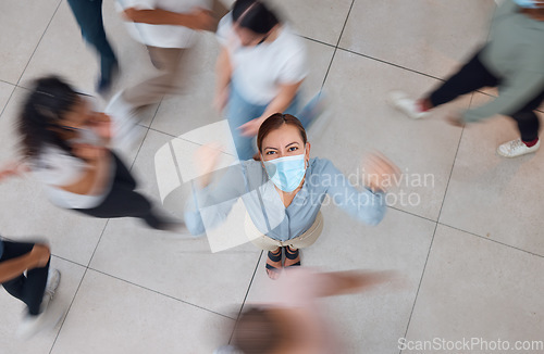 Image of Angry business woman with a mask for covid and people walking around her. Young girl wearing face mask in a crowd, frustrated and shaking her fist. Aerial view of upset female in mall or office