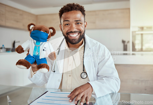 Image of Child doctor, pediatrician and healthcare work holding a teddy bear toy and looking happy and friendly while sitting in his office in a hospital. Health, care and smile of male medical physician