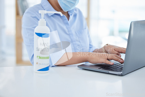 Image of Covid, hand sanitizer and a woman in office typing on laptop with face mask. Online work, hygiene and businesswoman with alcohol spray on desk. Virus prevention, safety and cleaning hands in pandemic