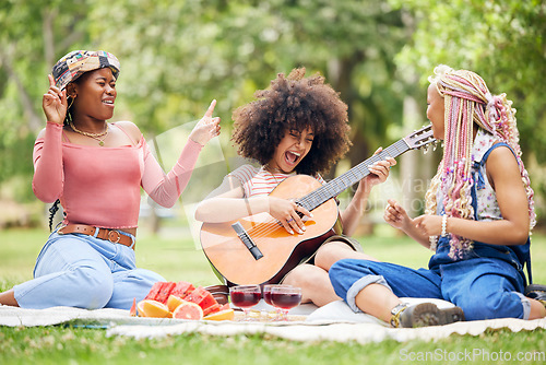 Image of Black women, friends and picnic in park with guitar playing music, singing and spending time together. Comic, funny and happy ladies with acoustic string instrument, food or wine outdoors for lunch.