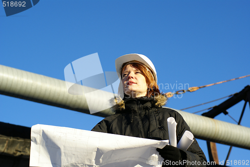 Image of Young architect looking at blueprint in front of construction si