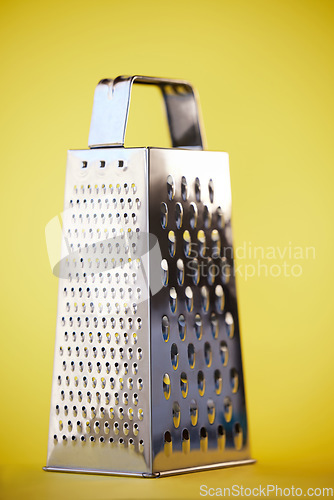Image of Metal or steel cheese grater for grocery cooking, food preparation and culinary help or support. Silver, metallic or home kitchenware appliance with cut pattern shredder isolated on yellow background