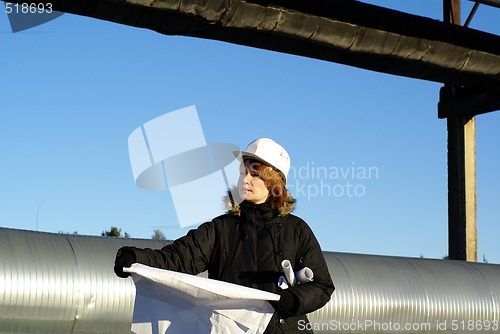 Image of Young architect looking at blueprint in front of construction si