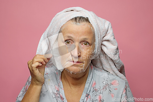 Image of senior woman applying a facial mask napkin